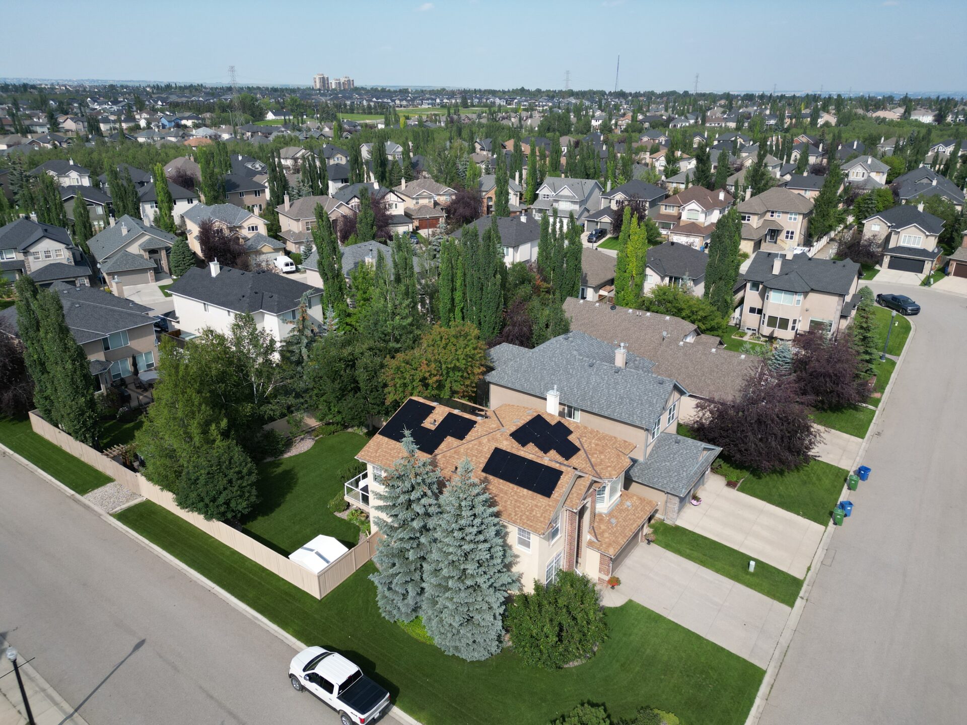 Aerial view of a suburban neighborhood with closely spaced houses, lush greenery, manicured lawns, and vehicles on clean streets.