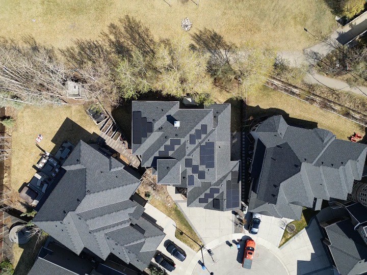 Aerial view of a residential neighborhood, capturing the intricate rooftops of houses, tree shadows, cars, and a well-trimmed lawn on a sunny day.