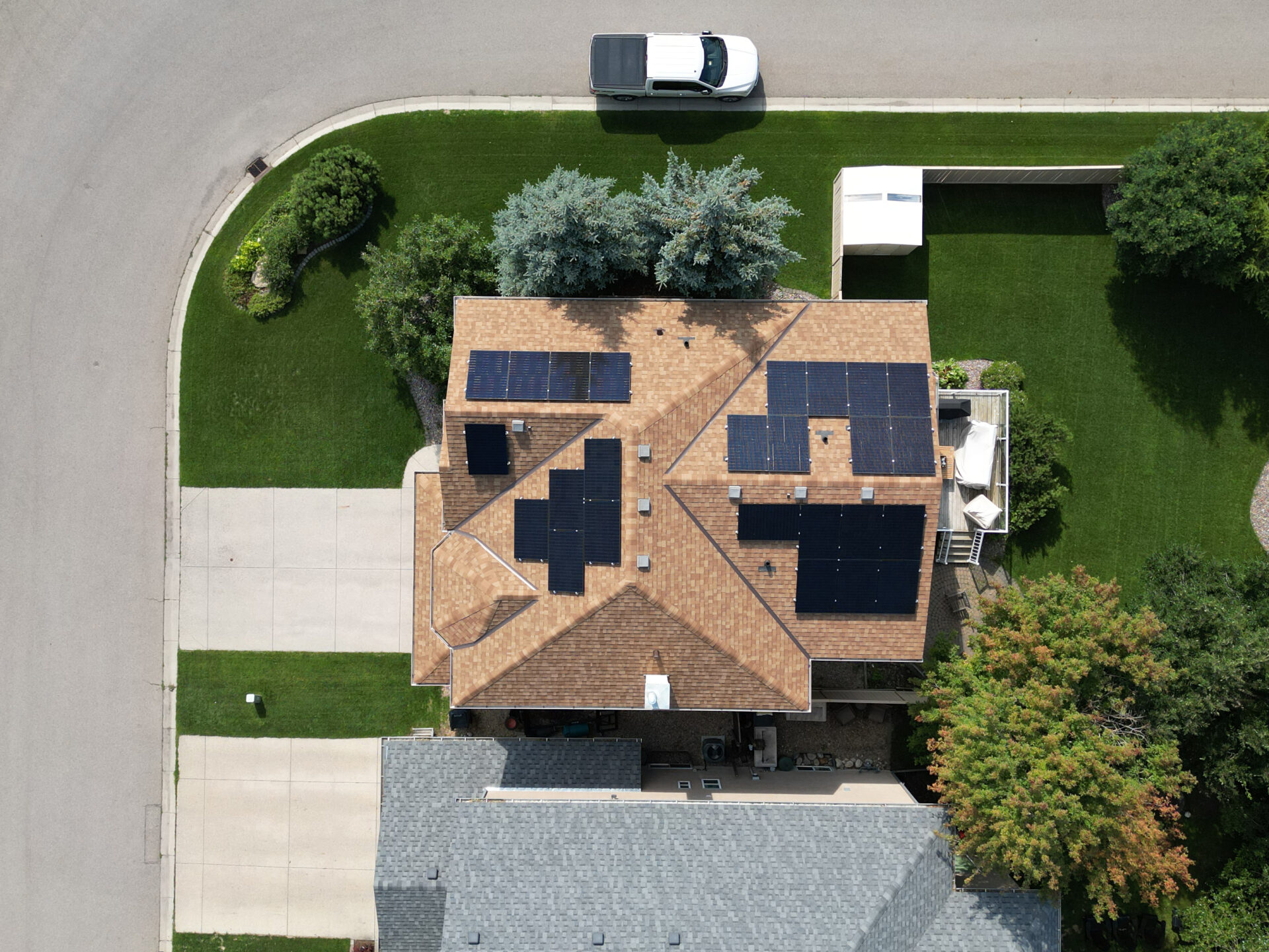 Aerial drone view of a high-efficiency residential solar panel installation on a dark-shingled roof in a Calgary neighborhood.