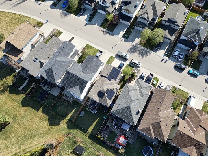 Aerial drone view of a residential Calgary neighborhood featuring houses with solar panel installations on shingle roofs.