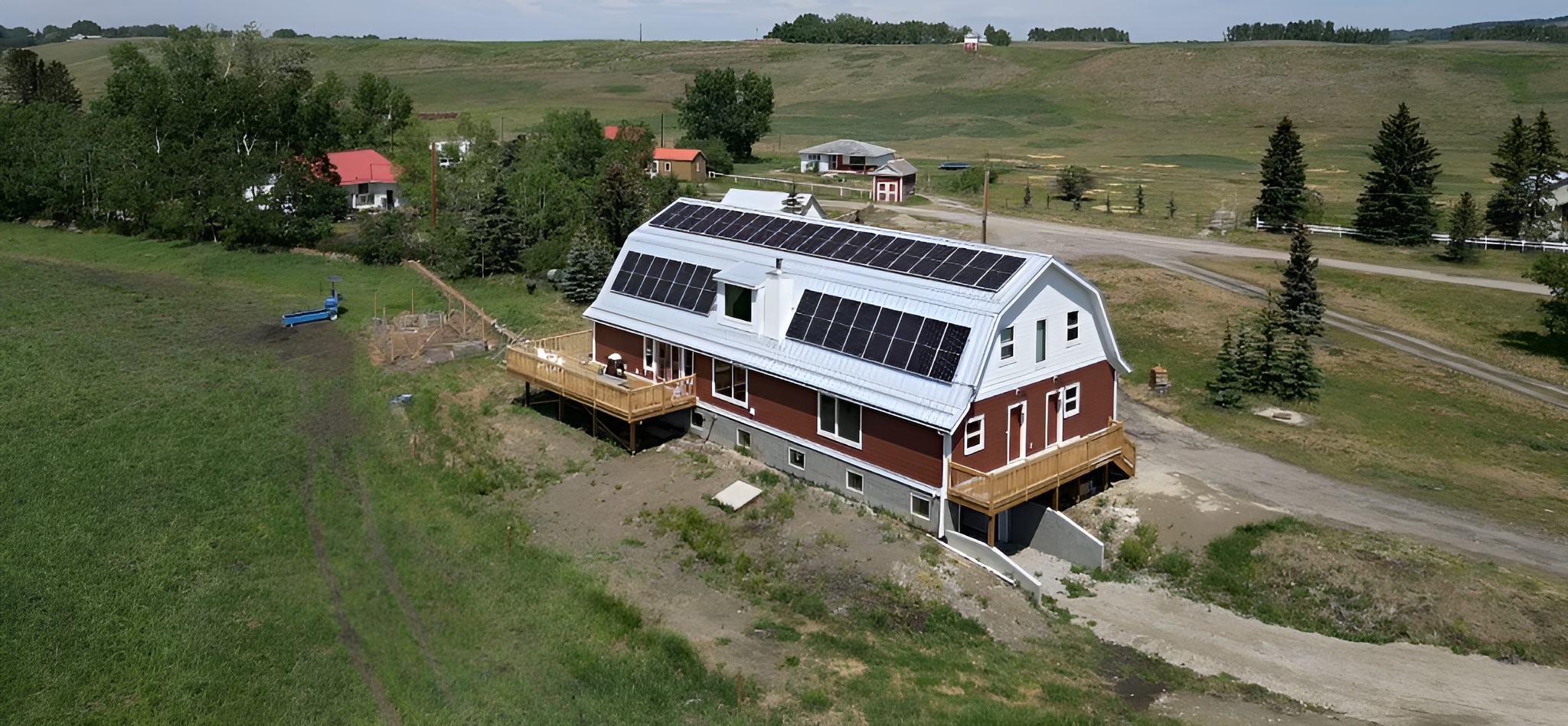 Aerial drone view of a custom residential and agricultural solar panel installation on a curved barn roof in the Alberta countryside by Rocky Mountain Solar Co.